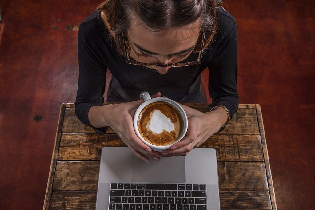One female student standing talking to a male and female student sitting on a brick wall on campus