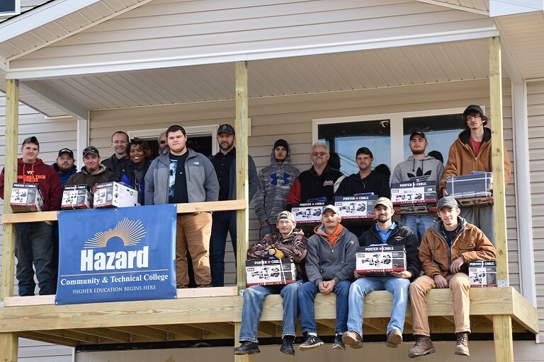 Large group of students posing in front of a wood cabin with the Hazard banner displayed in front of them
